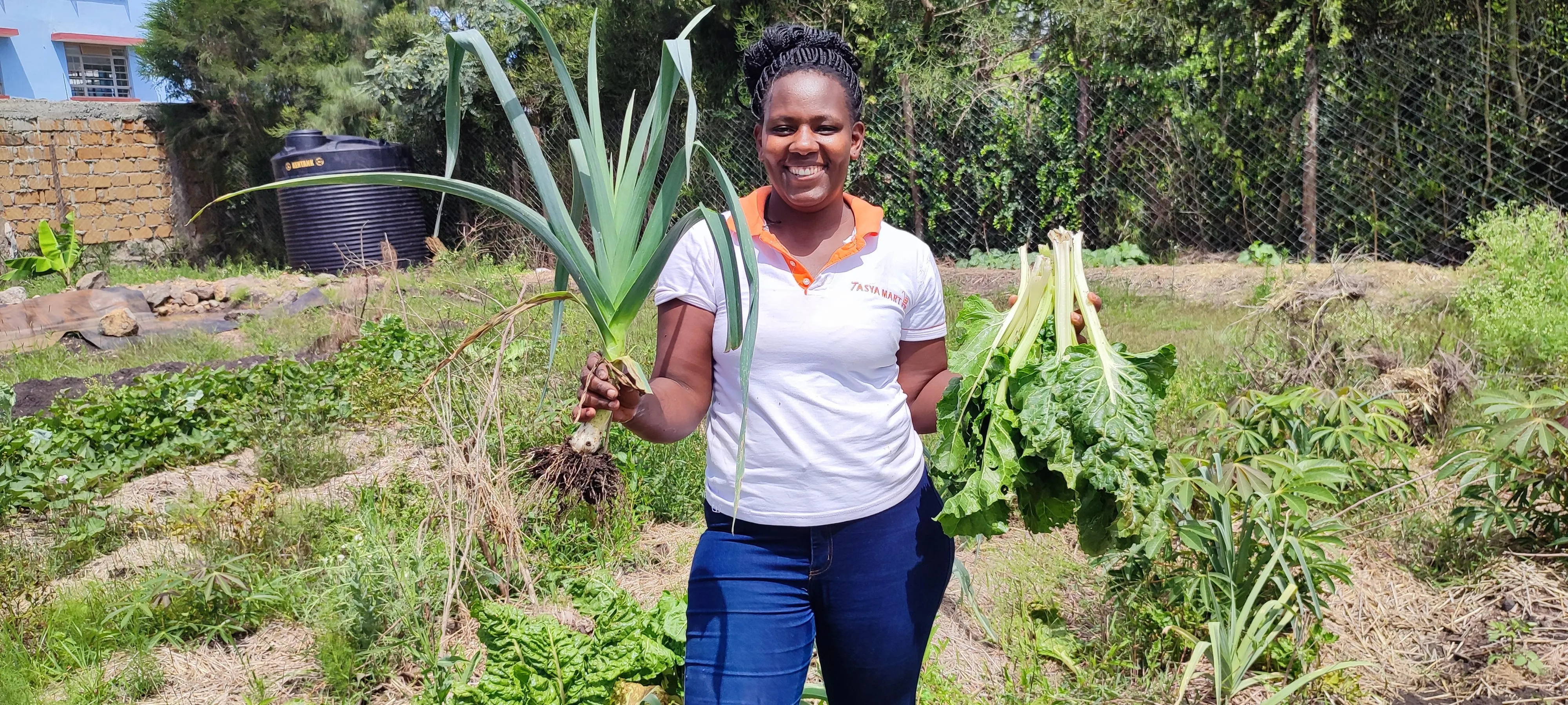 Ruth smiling in a garden, holding a freshly harvested leek and a bunch of chard.