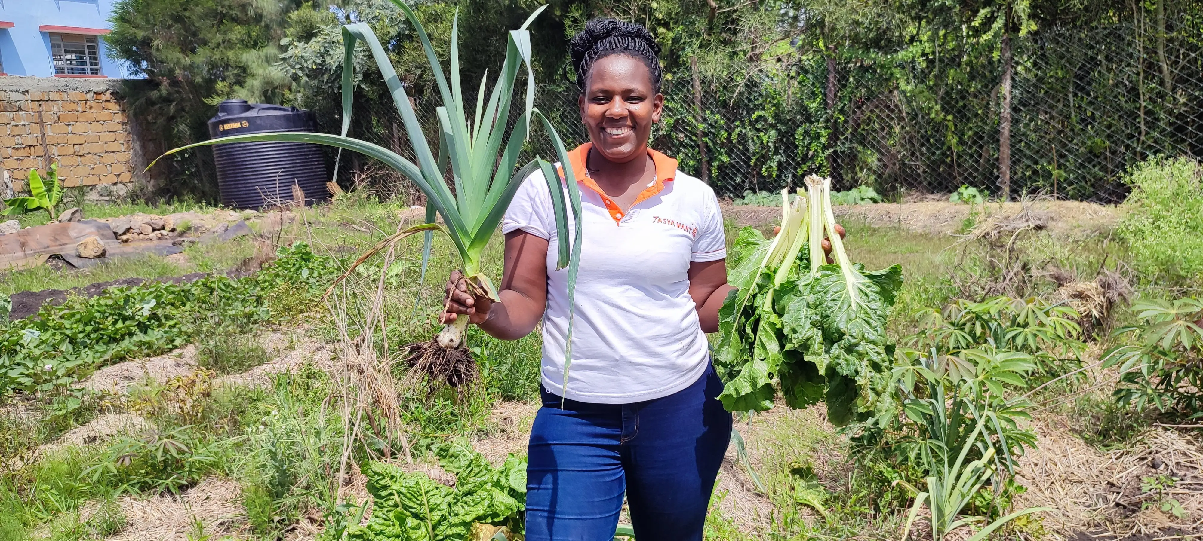 Ruth smiling in a garden, holding a freshly harvested leek and a bunch of chard.